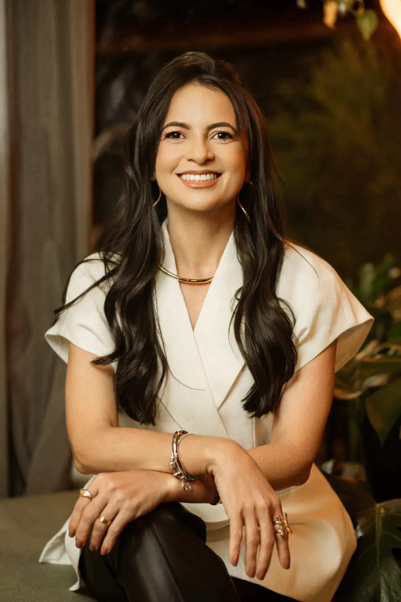 Cristiana Duarte, arquiteta especializada em espaços de saúde, sentada e sorrindo, com fundo de vegetação desfocada